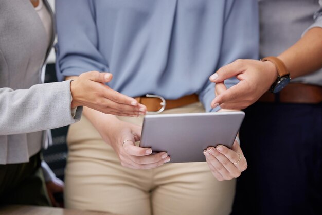 Echemos un vistazo Foto de un grupo de empresarios irreconocibles usando una tableta digital en una oficina en el trabajo