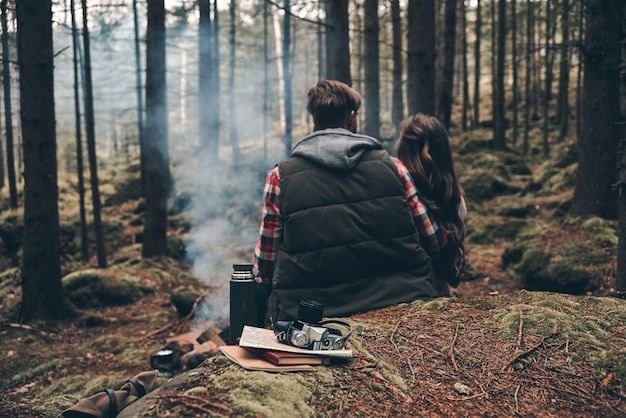 Echte Seelenverwandte. Rückansicht eines jungen Paares, das sich am Lagerfeuer aufwärmt, während es im Wald sitzt