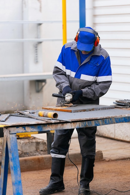 Echter Arbeiter in Overalls und Baseballmütze schleift Metalloberfläche Mann bei der Arbeit