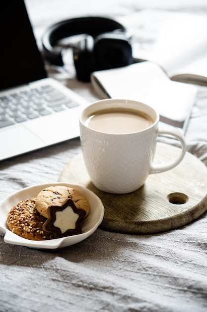 Echter Heimarbeitsplatz-Laptop mit Tasse Kaffee mit Keksen auf dem Bett mit gemütlicher Decke