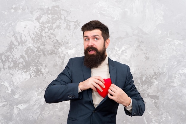 Echter Valentinsgruß ist mehr als nur Herz. Bärtiger Mann nimmt Herz aus der Tasche. Herzproblem oder -attacke. Herzschmerz und Brustschmerzen. Herz zum Valentinstag geben. Feiertag der Liebe und Fürsorge. Gesundheitswesen.