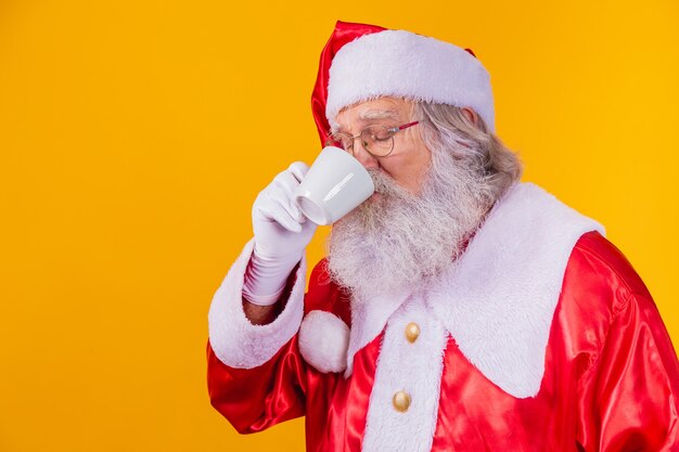 Echter Weihnachtsmann, der einen Kaffee auf gelbem Hintergrund mit freiem Platz für Text trinkt.