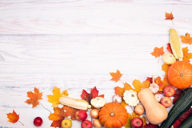 Ecklayout mit Kürbis, Mais, anderem Gemüse und Herbstlaub. Draufsicht auf einem hellen hölzernen Hintergrund. Herbst flach lag.