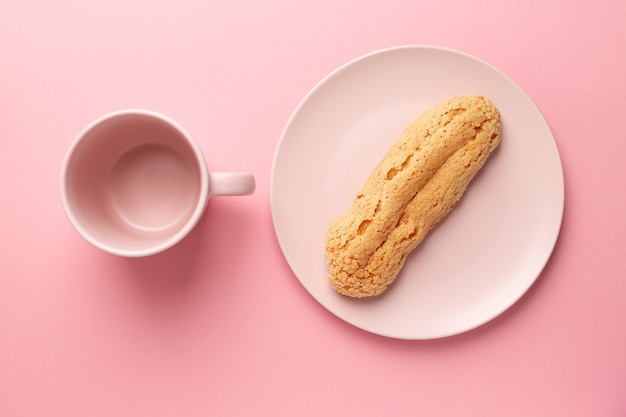 Eclair auf dem Teller. Rosa Pastellhintergrund. Dessert. Konzept, Minimalismus