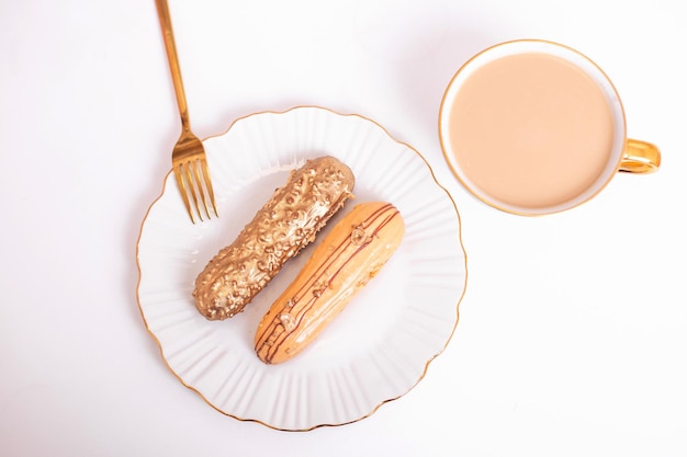 Eclairs de color dorado en plato, cuchillo y tenedor, taza de café