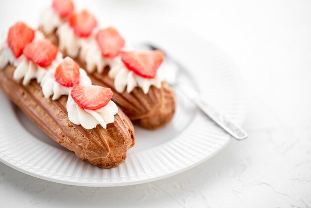 Foto eclairs com creme e morangos e uma chávena de chá num prato branco