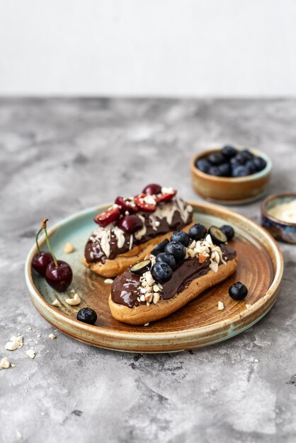 Eclairs com nozes e bagas de cobertura de chocolate em um fundo de concreto