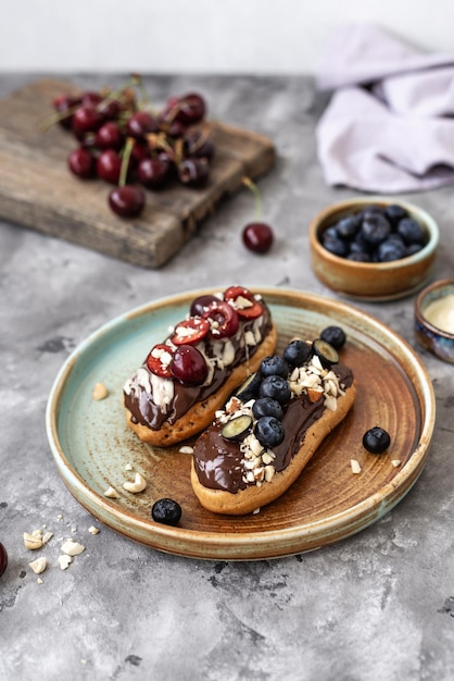 Eclairs com nozes e bagas de cobertura de chocolate em um fundo de concreto