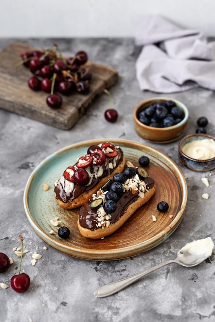 Eclairs com nozes e bagas de cobertura de chocolate em um fundo de concreto