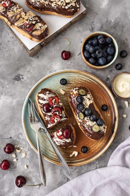 Eclairs com nozes e bagas de cobertura de chocolate em um fundo de concreto