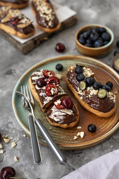 Eclairs com nozes e bagas de cobertura de chocolate em um fundo de concreto