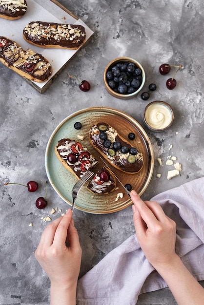 Eclairs com nozes e bagas de cobertura de chocolate em um fundo de concreto