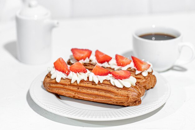 Eclairs con crema y fresas y una taza de café en un plato blanco