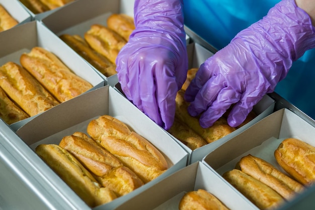 Eclairs, die in weißen Kartons liegen Hände in Handschuhen berühren Gebäck Lebensmittel müssen gut verpackt sein Halten Sie sich an Hygienestandards