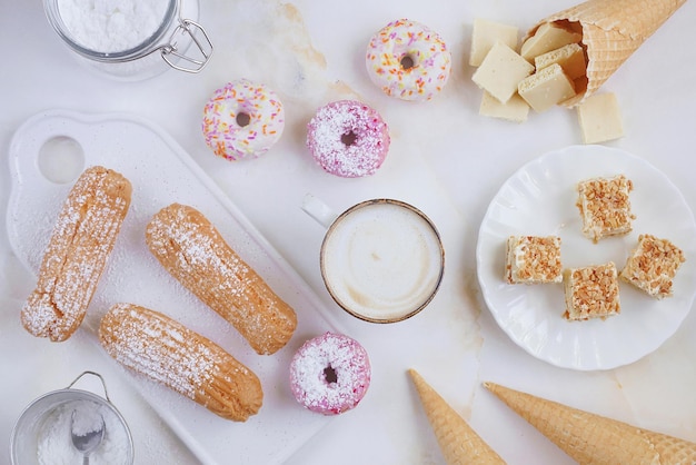 Eclairs y donuts con café sobre un fondo de mármol, Fondo claro, Confitería al estilo de un blogger