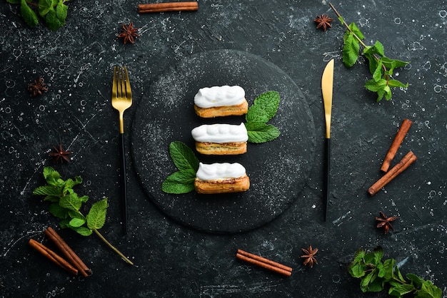 Eclairs dulces y deliciosos con crema en un plato negro con menta Vista superior Estilo rústico