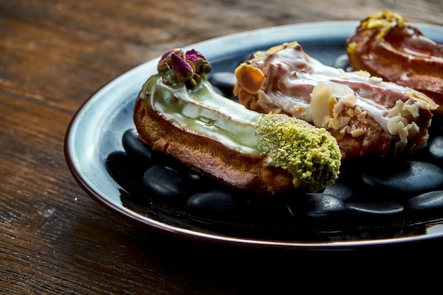 Eclairs franceses con natillas y coberturas variadas servidas en una placa negra sobre un fondo de madera. Comida de restaurante.