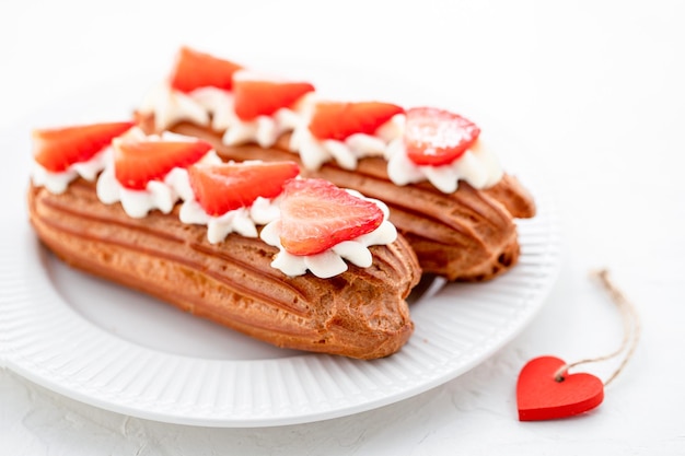 Eclairs mit Sahne und Erdbeeren auf einem weißen Teller Valentinstag-Konzept