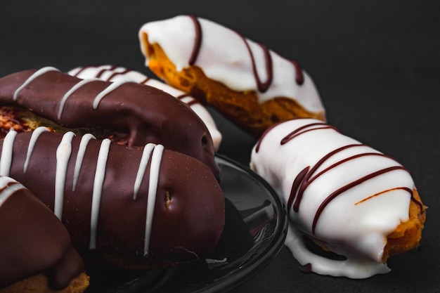Foto eclairs mit schokoladenfüllung und weißer schokolade auf schwarzer oberfläche.