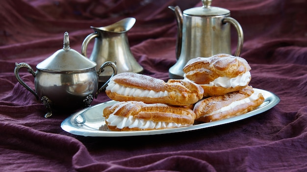 Eclairs, pastas choux rellenas con crema batida, fondo violeta oscuro, vajilla de plata