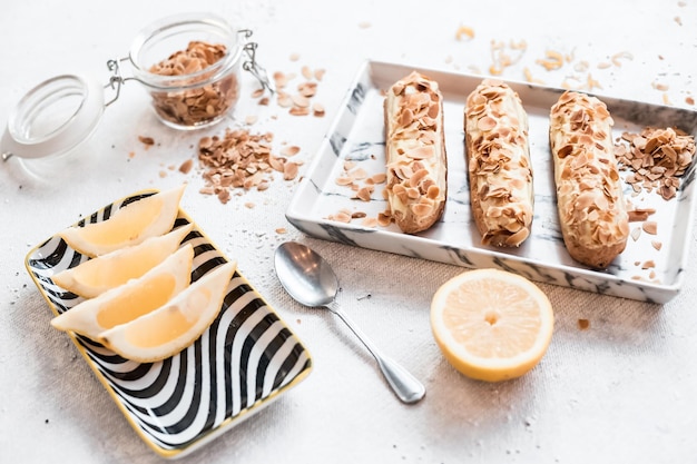 Eclairs de postre francés tradicional con almendras en una composición sobre una mesa blanca y un plato junto a una rodaja de limón Tomada de una cafetería o restaurante