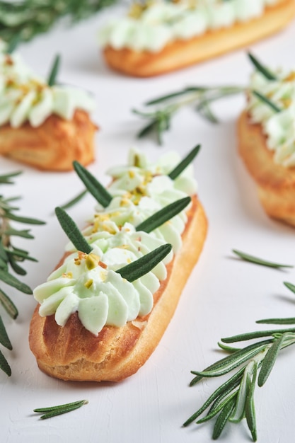 Eclairs con relleno de crema de pistacho y frambuesa, aderezado con pistacho triturado y romero.