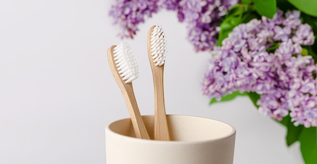 Eco cepillo de dientes de bambú en una taza con flores de color lila sobre fondo blanco. Copia espacio