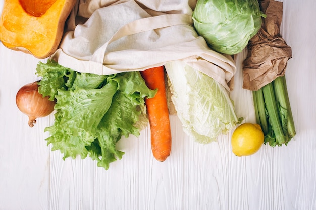 Eco plano plano de vegetais, verdes, embrulhados em papel em um saco de pano. Alface, repolho, aipo, cenoura, abóbora, limão, manjericão. Desperdício zero, sem plástico Conceito ecológico.