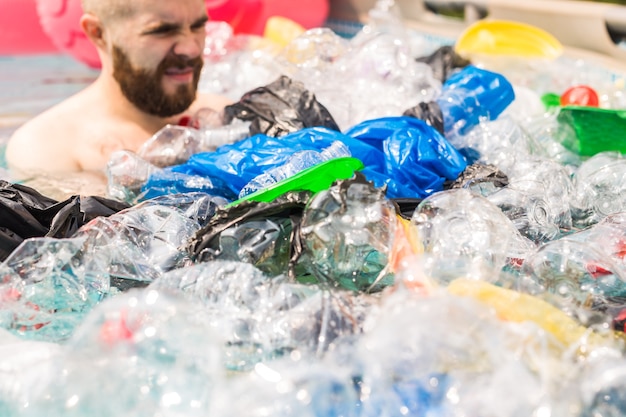 Ecologia, lixo plástico, emergência ambiental e poluição da água - homem chocado nadando em uma piscina suja.