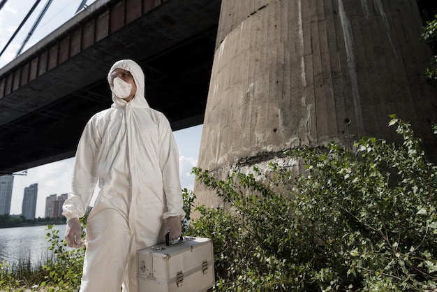 Ecologista em traje de proteção com kit de inspeção em pé perto da ponte