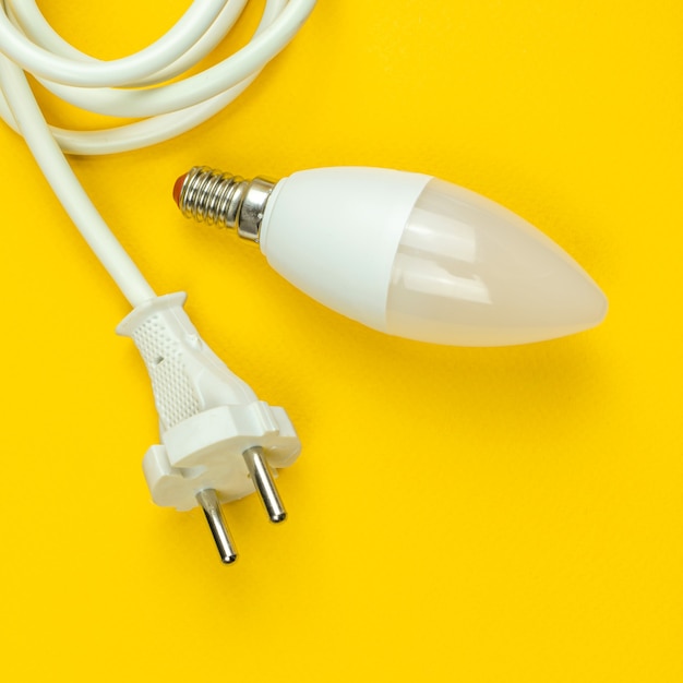 Economia de energia, conceito ecológico. Lâmpada LED e cabo de alimentação elétrica, fundo amarelo, design quadrado, vista superior e plano com foto do espaço da cópia