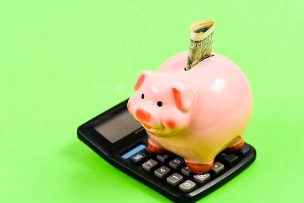 Economía y Finanzas. Calculadora y billetes de dólar rellenos de cerdo rosado de la alcancía. Bienestar financiero. Cuenta de ahorros. Ahorro de dinero. El depósito de ahorros es una forma conveniente y flexible de depositar ahorros.