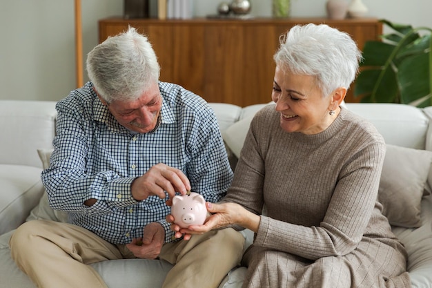 Economizando dinheiro para o futuro casal adulto sênior segurando o cofrinho colocando moeda de dinheiro