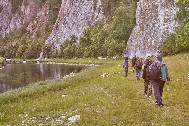 Ecoturismo en zona montañosa, grupo de cinco excursionistas caminando por sendero forestal a lo largo del río con costas rocosas.