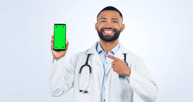 Ecrã verde do telefone e retrato do médico apontando para promoção ou registro em fundo branco Cuidados de saúde de estúdio ou sinal para oferecer informações ou serviços ou apresentação de aplicativos móveis de tele-saúde