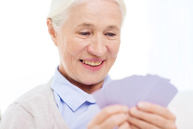 edad, juego, apuesta, póquer y concepto de la gente - anciana sonriente feliz jugando a las cartas en casa