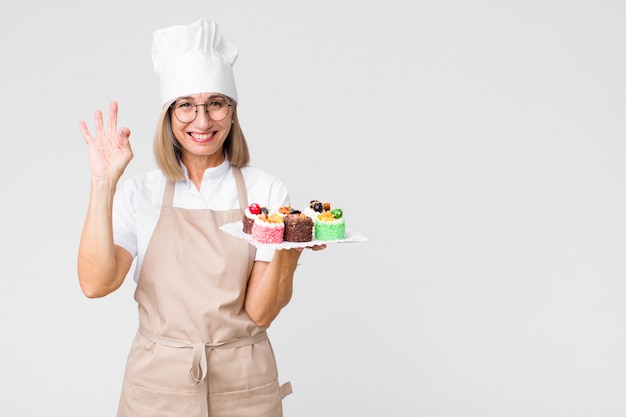 Edad media bonita mujer panadero con pasteles contra la pared del espacio de copia