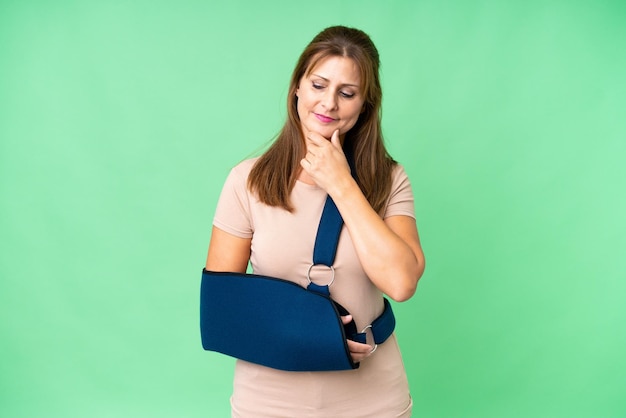 Edad media con un brazo roto y un cabestrillo sobre un fondo aislado mirando hacia un lado y sonriendo