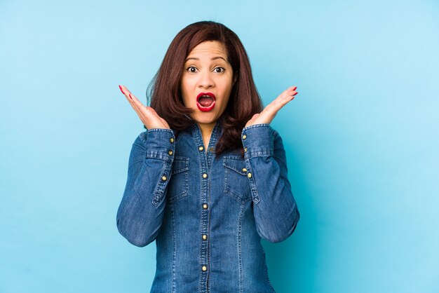 Edad media mujer latina aislada en azul sorprendido y conmocionado.