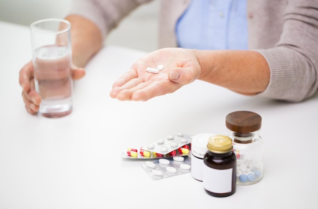 la edad, la medicina, la atención de la salud y el concepto de la gente: el cierre de una anciana con pastillas y un vaso de agua en casa