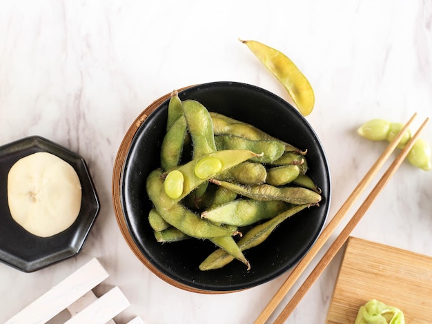 Edamame al vapor en un tazón negro sobre una mesa blanca de mármol con espacio para copiar