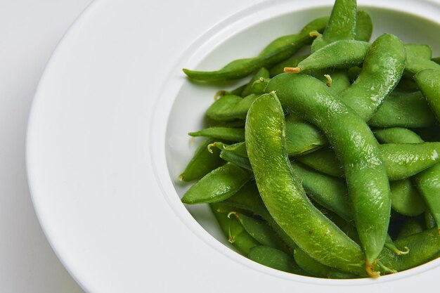 Edamame japonês quente servido em prato branco, menu de aperitivos