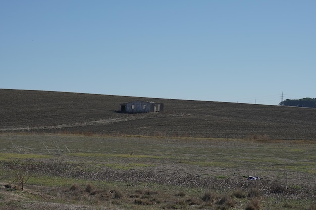 Foto edifício abandonado isolado em meio a extensos campos castanhos sob um céu azul claro