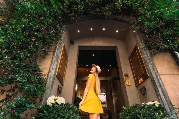 Edificio con un arco y una puerta de cristal La chica con un elegante vestido amarillo posa