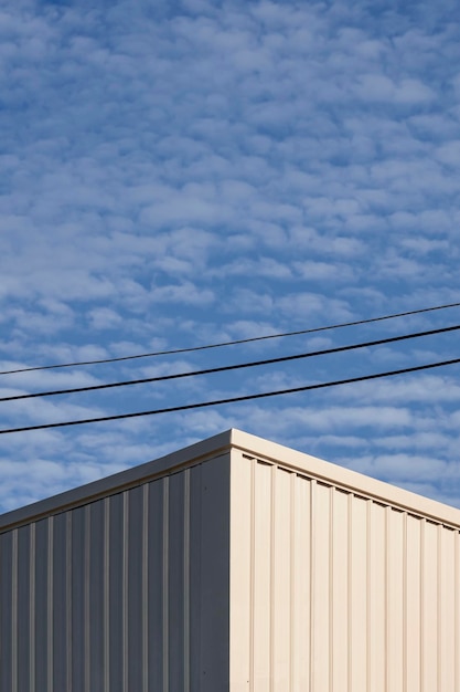 Edifício industrial de aço ondulado branco com linhas de energia contra nuvens fofas no céu azul