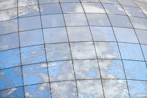 Edificio moderno esférico de cristal con reflejo de cielo azul y nubes.