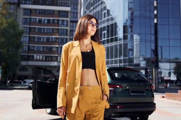 Edificio de negocios moderno en el fondo Mujer de moda joven en abrigo de color burdeos durante el día con su coche