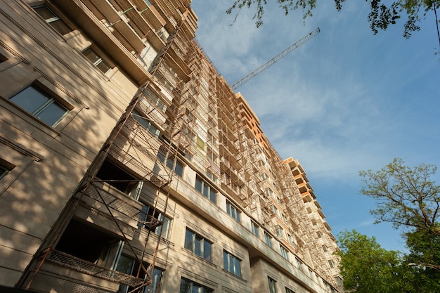 Edifício residencial de vários andares em construção e guindaste em um fundo de céu azul