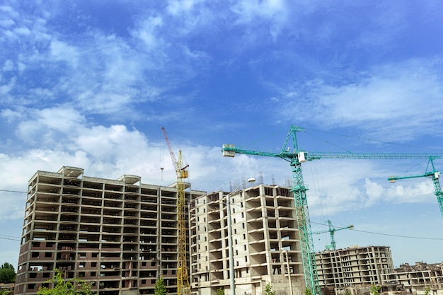 Edifício residencial de vários andares em construção e guindaste em um fundo de céu azul