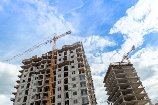 Edifício residencial de vários andares em construção e guindaste em um fundo de céu azul